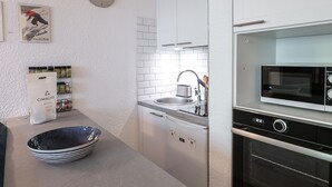 Eine moderne Küche mit weißen Schränken, einer Mikrowelle, einem Backofen, einem Spülbecken und einer Uhr mit Chili-Motiv.