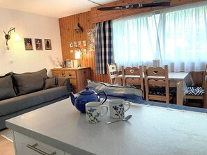 A cozy room with a sofa, a table with a kettle and mugs, wooden walls, and a dining area.