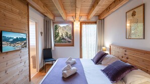 Habitación de cabaña de madera con una cama, una silla, un televisor y un ventanal con vistas a la montaña.