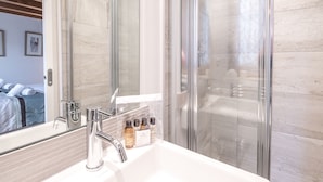 Un baño moderno con cabina de ducha de vidrio, un espejo grande y un lavabo con artículos de aseo.