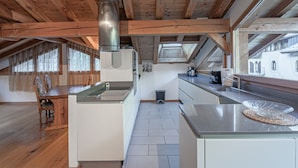 Una cocina moderna con vigas de madera, una isla central y vistas a un edificio a través de un amplio ventanal.