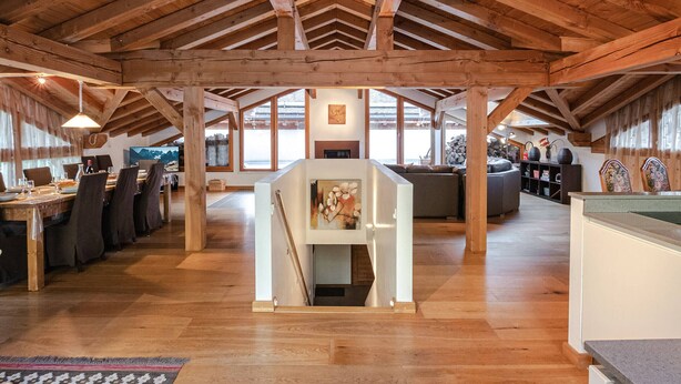 Un loft espacioso con techos altos y vigas de madera a la vista. Cuenta con una chimenea central, un comedor con una mesa larga y sillas, y un área de estar con sofás.