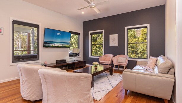 A modern living room with a flat-screen TV, two sofas, a coffee table, and large windows with a view of trees. - Seaclusion ... walk to the Beach, Lake or the The Recky! (Elizabeth Beach)