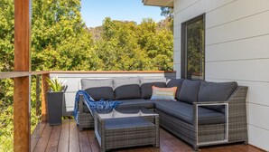 A modern outdoor seating area with a grey sectional sofa, a small table, and a wicker coffee table. - Seaclusion ... walk to the Beach, Lake or the The Recky! (Elizabeth Beach)