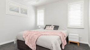 Une chambre à coucher avec un lit, des tables de chevet et des fenêtres équipées de stores.