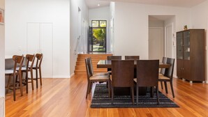 A modern dining area with a wooden table and chairs, a dark rug, and a staircase leading to a balcony with a view of greenery. - Seaclusion ... walk to the Beach, Lake or the The Recky! (Elizabeth Beach)