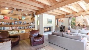 A spacious living room with a fireplace, wooden bookshelves, leather armchairs, and a grey sofa.
