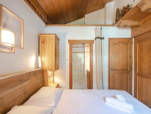 Quarto com cabeceira de madeira, cama com roupa de cama branca, mesa de cabeceira com abajur e portas de madeira.