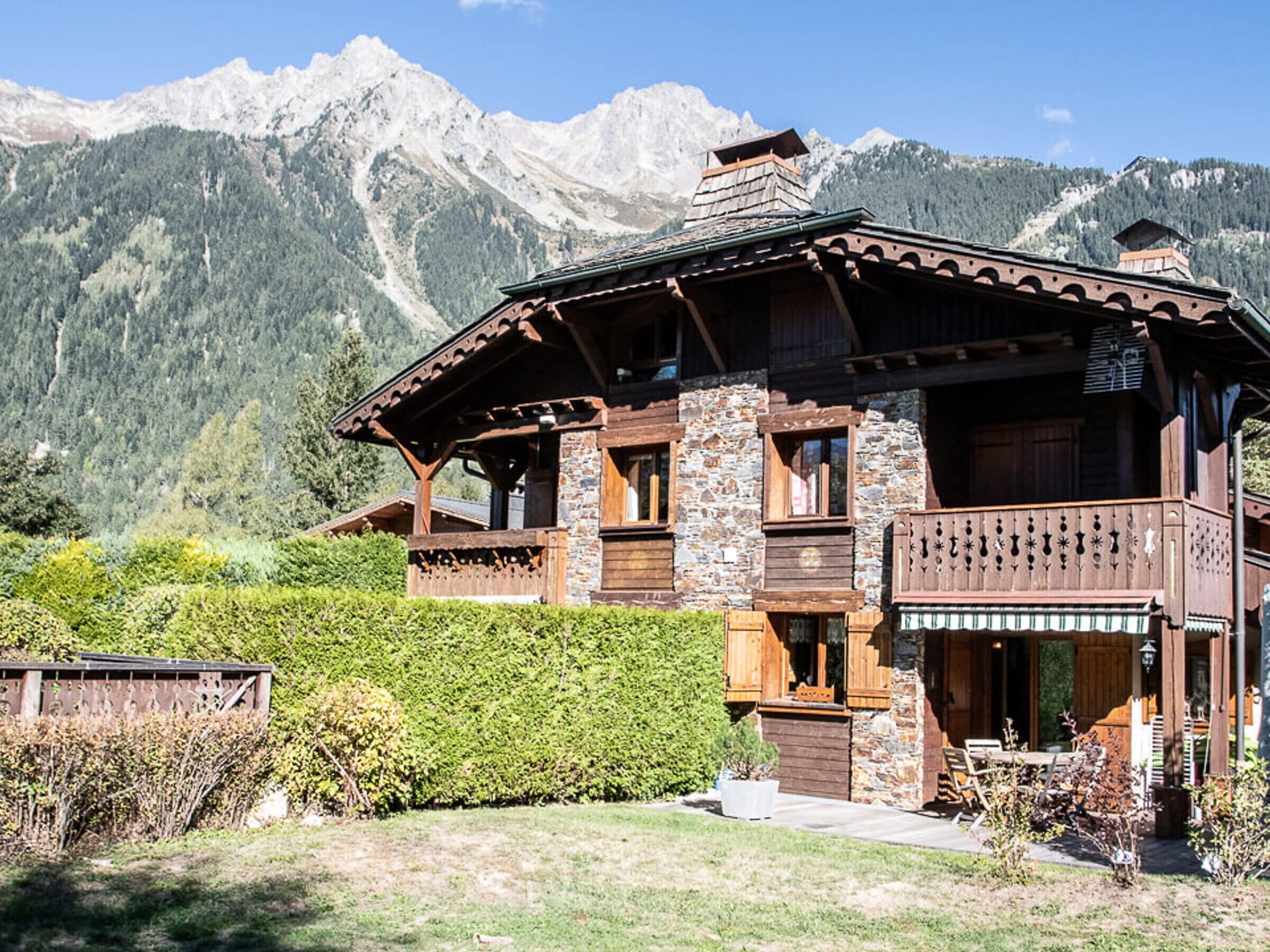 Un chalet doté d’une façade en pierre, de balcons en bois et surplombant un paysage montagneux.