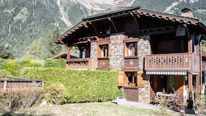 Un chalet doté d’une façade en pierre, de balcons en bois et surplombant un paysage montagneux.