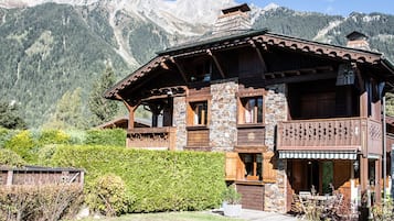 Un chalet doté d’une façade en pierre, de balcons en bois et surplombant un paysage montagneux.