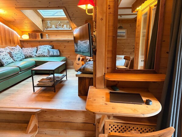 A cozy cabin interior with a sofa, coffee table, TV, and a dining area. - Beautiful duplex with garden in Chamonix, 4 people, pets allowed, parking, wifi (Chamonix-Mont-Blanc)