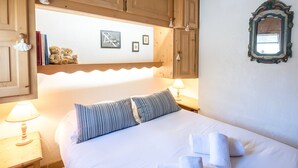 Une chambre avec des armoires en bois, un lit avec des coussins à rayures, une lampe de chevet et des tableaux encadrés au mur.