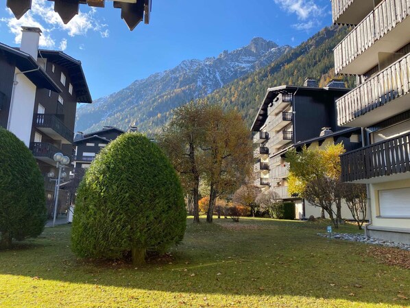 A residential area with a mountain backdrop, featuring multi-story buildings with balconies, a well-maintained lawn, and a clear sky.