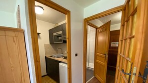 A narrow hallway with wooden doors leading to a kitchen and a bathroom.