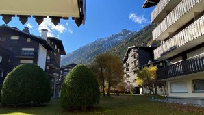 A courtyard with a mountain backdrop, featuring a building with balconies and a well-maintained lawn.