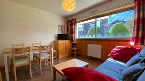 A cozy room with a wooden dining table, chairs, a sofa, and a TV on a wooden cabinet.