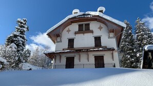 Un edificio de dos pisos con techo inclinado, balcones de madera y un paisaje cubierto de nieve.