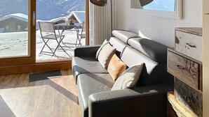 Uma sala de estar moderna com um sofá de couro, um armário de madeira e vista para montanhas cobertas de neve através de grandes janelas.