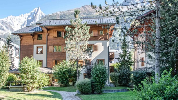 A multi-story building with a wooden facade, a brick pathway, and a mountainous backdrop. - Spacious 6-room apartment for 10 near slopes, pets OK, parking, WiFi (Chamonix-Mont-Blanc)