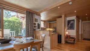 A spacious kitchen with wooden cabinets, a dining area with a table and chairs, and a view of the outdoors through large windows. - Spacious 6-room apartment for 10 near slopes, pets OK, parking, WiFi (Chamonix-Mont-Blanc)