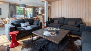 A modern living room with two sofas, a coffee table, and a red stool. There is a dining area with a table and chairs visible through a window. - Spacious 6-room apartment for 10 near slopes, pets OK, parking, WiFi (Chamonix-Mont-Blanc)