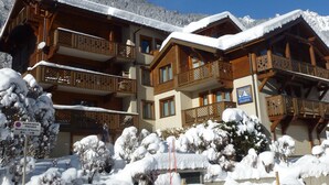 A multi-story chalet with wooden balconies and a sign indicating a ski resort. - Spacious 6-room apartment for 10 near slopes, pets OK, parking, WiFi (Chamonix-Mont-Blanc)