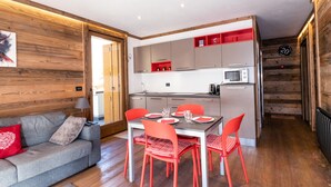 Une cuisine compacte dotée d’appareils électroménagers modernes, un coin repas avec des chaises rouges et un canapé gris agrémenté de coussins rouges.