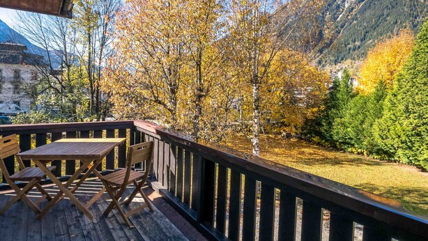 Une terrasse en bois avec une table et des chaises, offrant une vue sur un paysage montagneux aux couleurs automnales.