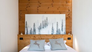 Un lit bien fait, avec deux oreillers, une grande peinture représentant une forêt accrochée au mur au-dessus, et une tête de lit en bois.