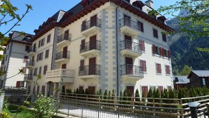 Un immeuble à plusieurs étages, doté de balcons et d’une façade blanche, avec une chaîne de montagnes en arrière-plan.