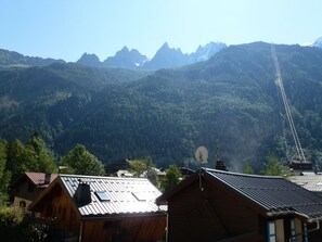 A mountain village with traditional wooden houses, a clear sky, and a mountain range in the background.