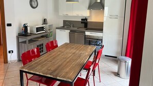 Une cuisine de taille réduite avec des meubles blancs, une table à manger en bois, des chaises rouges, un four à micro-ondes, une bouilloire et une horloge au mur.