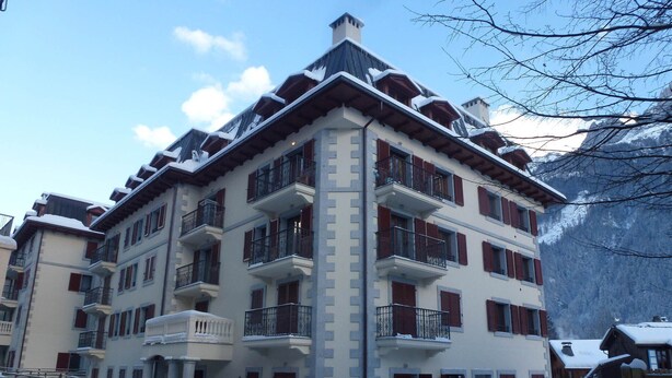 Un hôtel à plusieurs étages doté de balcons, dont la façade est recouverte de neige, et qui se dresse sur fond de montagnes.