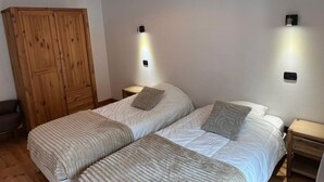 Une chambre avec deux lits, une armoire en bois, des tables de chevet et des lampes fixées au mur.