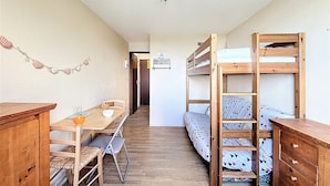 A compact room with a bunk bed, a wooden desk, a dining table with chairs, and a ceiling light fixture.