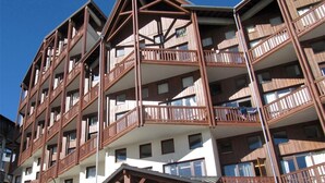 A multi-story hotel with balconies, a stone base, and a ski slope view. - Renovated Duplex - Sleeps 6 - Ski-in/Ski-out - Mountain View Balcony - Close to Shops (Val Thorens)
