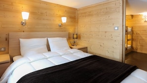 A wooden-paneled room with a bed, two wall-mounted lights, and a nightstand. - Renovated Duplex - Sleeps 6 - Ski-in/Ski-out - Mountain View Balcony - Close to Shops (Val Thorens)
