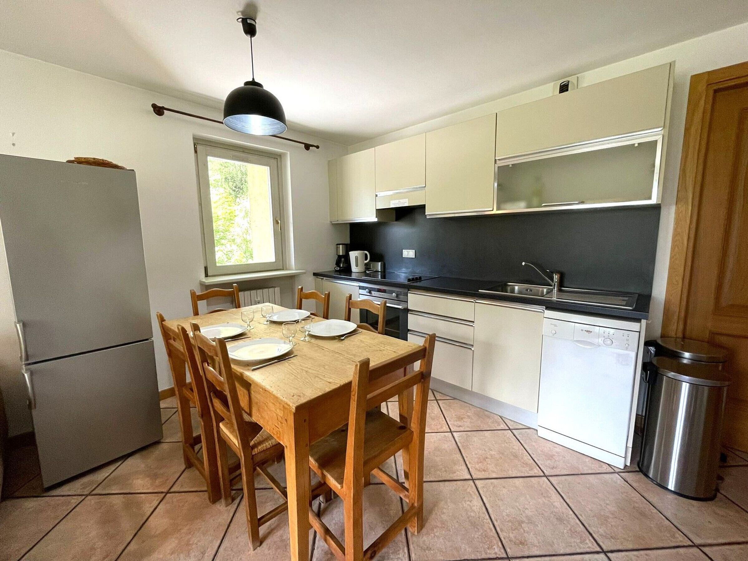 Une cuisine compacte comprenant une table à manger pour quatre personnes, un réfrigérateur, un évier et un lave-vaisselle.
