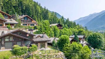 A mountain village with wooden houses, a stone wall, and a view of the valley.