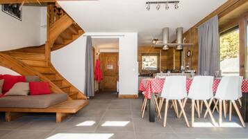 A modern interior with a wooden staircase, a dining area with a red and white checkered tablecloth, and a kitchen visible through an open door.