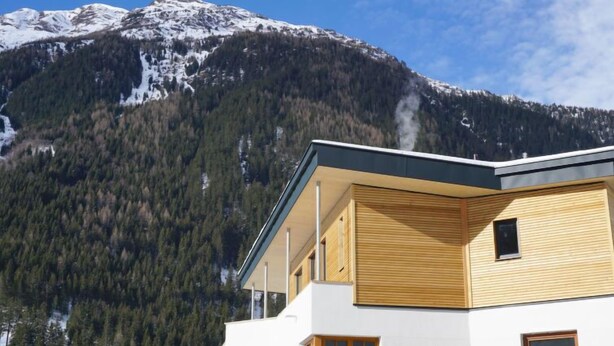 Ein modernes Gebäude mit Balkon, umgeben von bewaldeten Bergen.