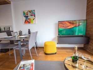 A modern living room with a dining area, a flat-screen TV, a magazine, and a bottle of Henkell Tröcken champagne. - Modern apartment with balcony and parking in Chamonix (Chamonix-Mont-Blanc)