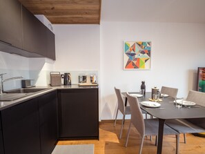 A modern kitchen with dark cabinetry, a wooden ceiling, and a dining area with a table and chairs. - Modern apartment with balcony and parking in Chamonix (Chamonix-Mont-Blanc)