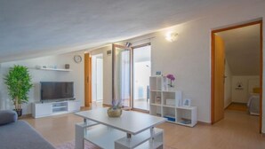 A modern living room with a flat-screen TV, a sofa, a coffee table, and a potted plant. There is a sliding glass door leading to a balcony. - Wind Soleil by Interhome (Jablanac)
