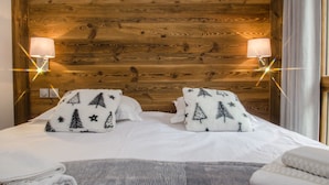 Een hotelkamer met een houten hoofdbord, twee bedlampen, een bed met witte lakens en twee decoratieve kussens met boommotieven.