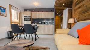 Een moderne keuken met houten kastjes, een eethoek met stoelen en een tafel, en een zithoek met een bank en kussens.