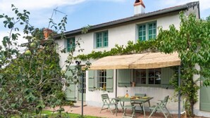 A house with a patio area featuring a table and chairs, surrounded by greenery and a thatched roof. - Le Glaude by Interhome (Chiddes)