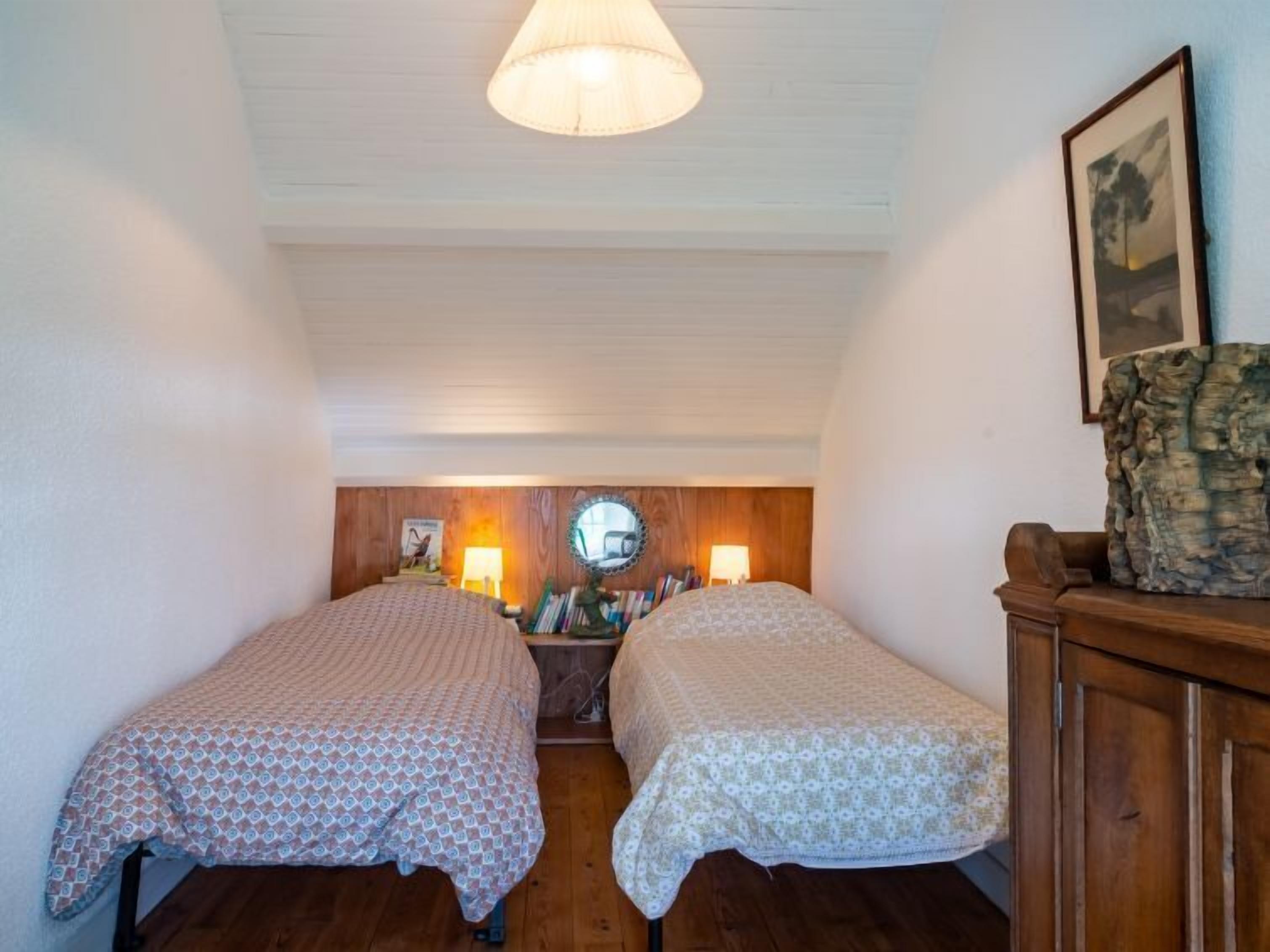 A room with two beds, wooden flooring, a wooden cabinet, and a mirror on the wall.