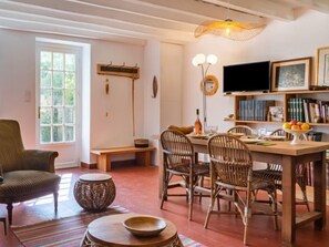 A cozy living room with a dining area, featuring wicker furniture, a television, and a bookshelf. - Le Glaude by Interhome (Chiddes)